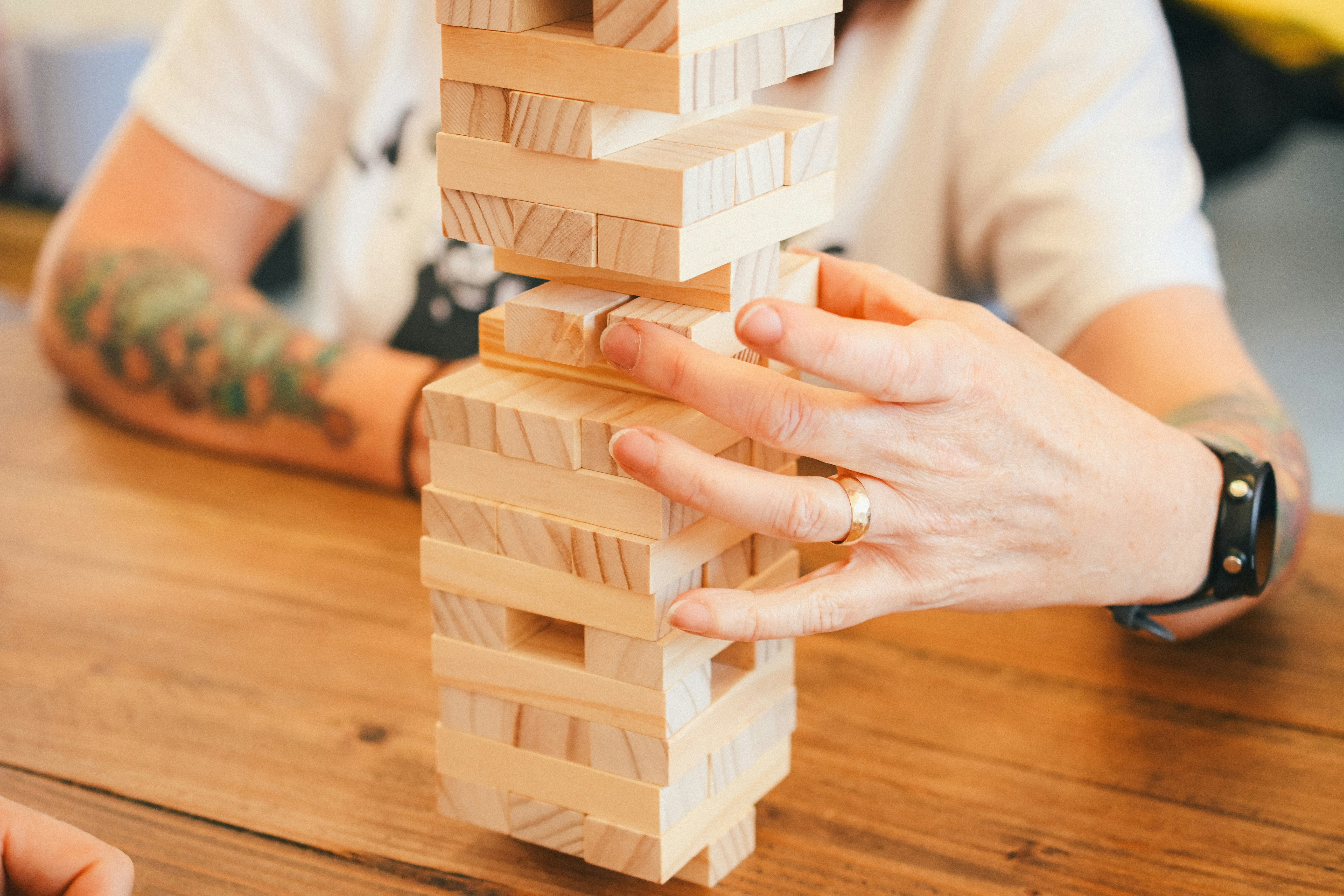 •	A close-up of someone removing a stabilising block from a carefully stacked structure (Jenga-style metaphor), symbolising small cuts destabilising the whole.